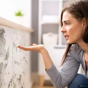 Frau kniet vor schimmelnder Wand