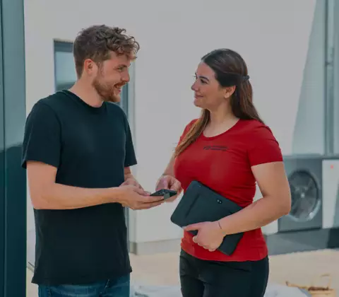 Fachhandwerker spricht mit Endkunde im Garten, im Hintergrund WOLF Wärmepumpe